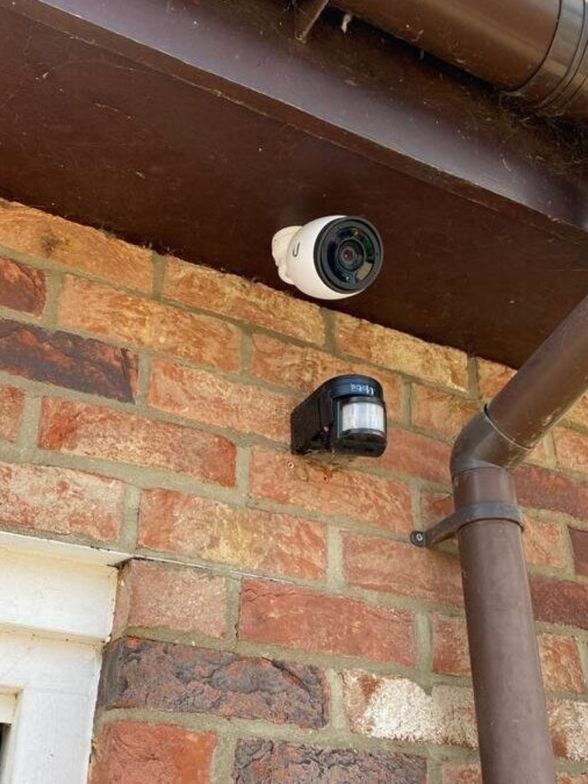 UniFi security camera mounted on the side of a brick house pointing downwards