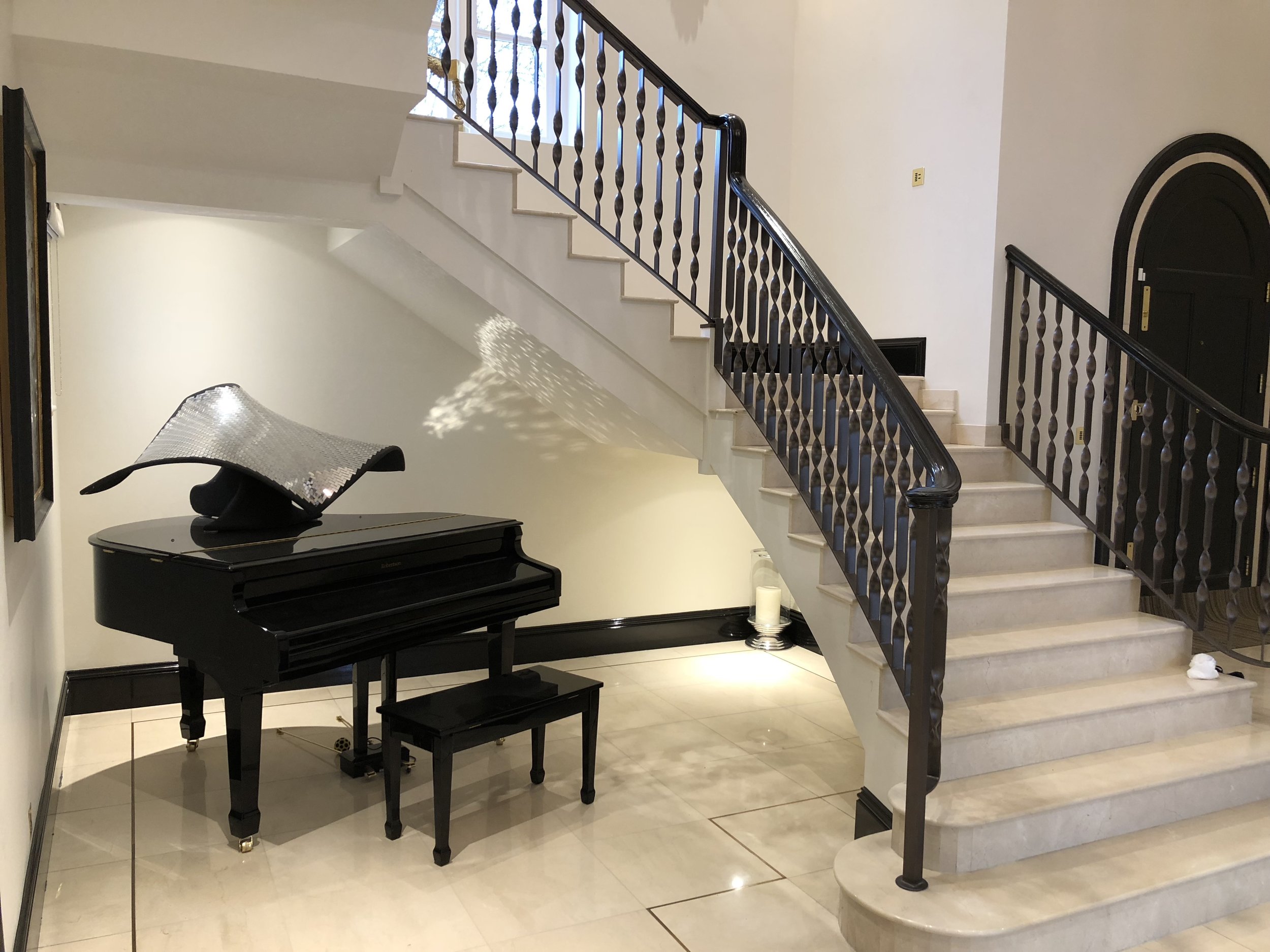 Large hallway with sweeping stairs, piano under the stairs and wall mounted Rako keypad on the stairs