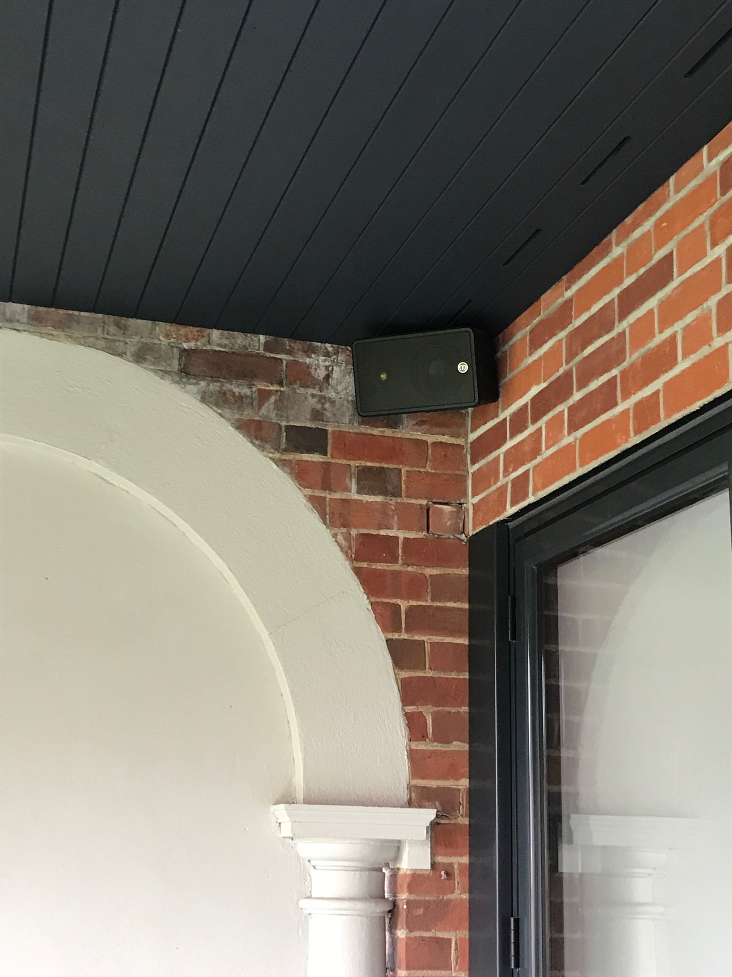 Close up of Monitor Audio speaker mounted to outside brick wall