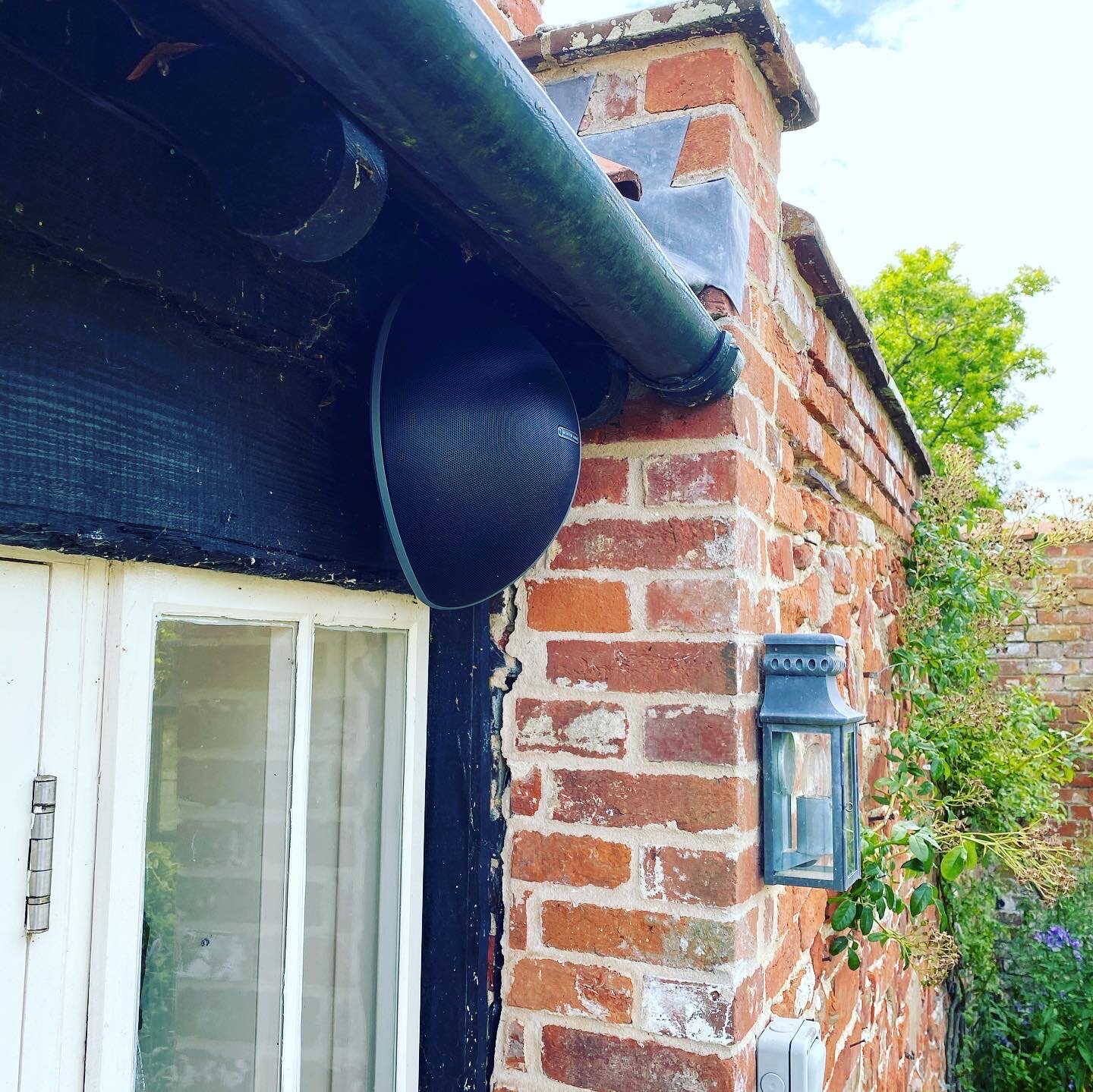 Monitor Audio speaker mounted to a brick wall on the outside of a property.