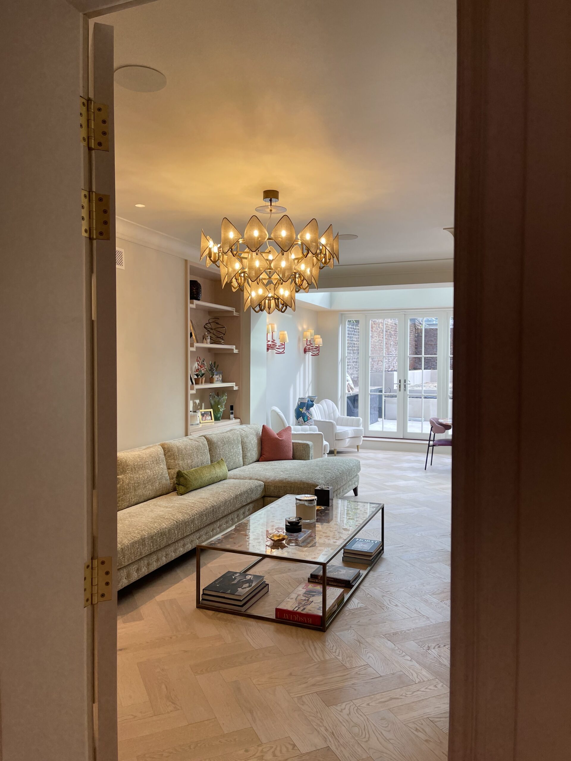 Door opening on a living area with parquet flooring, statement chandelier and in-ceiling speakers